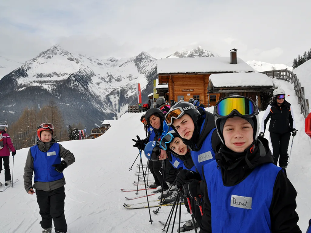 Jugendliche posieren mit Helm und Skibrille vor der Bergkulisse.